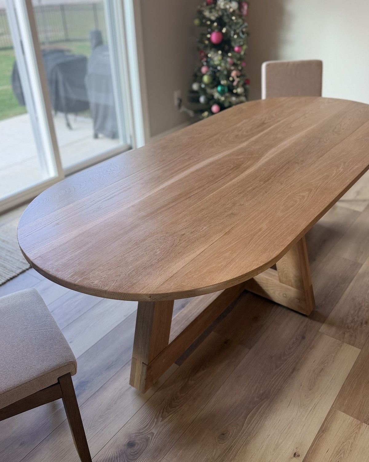 Oval white oak dining table with an angled trestle base in a sunlit dining room