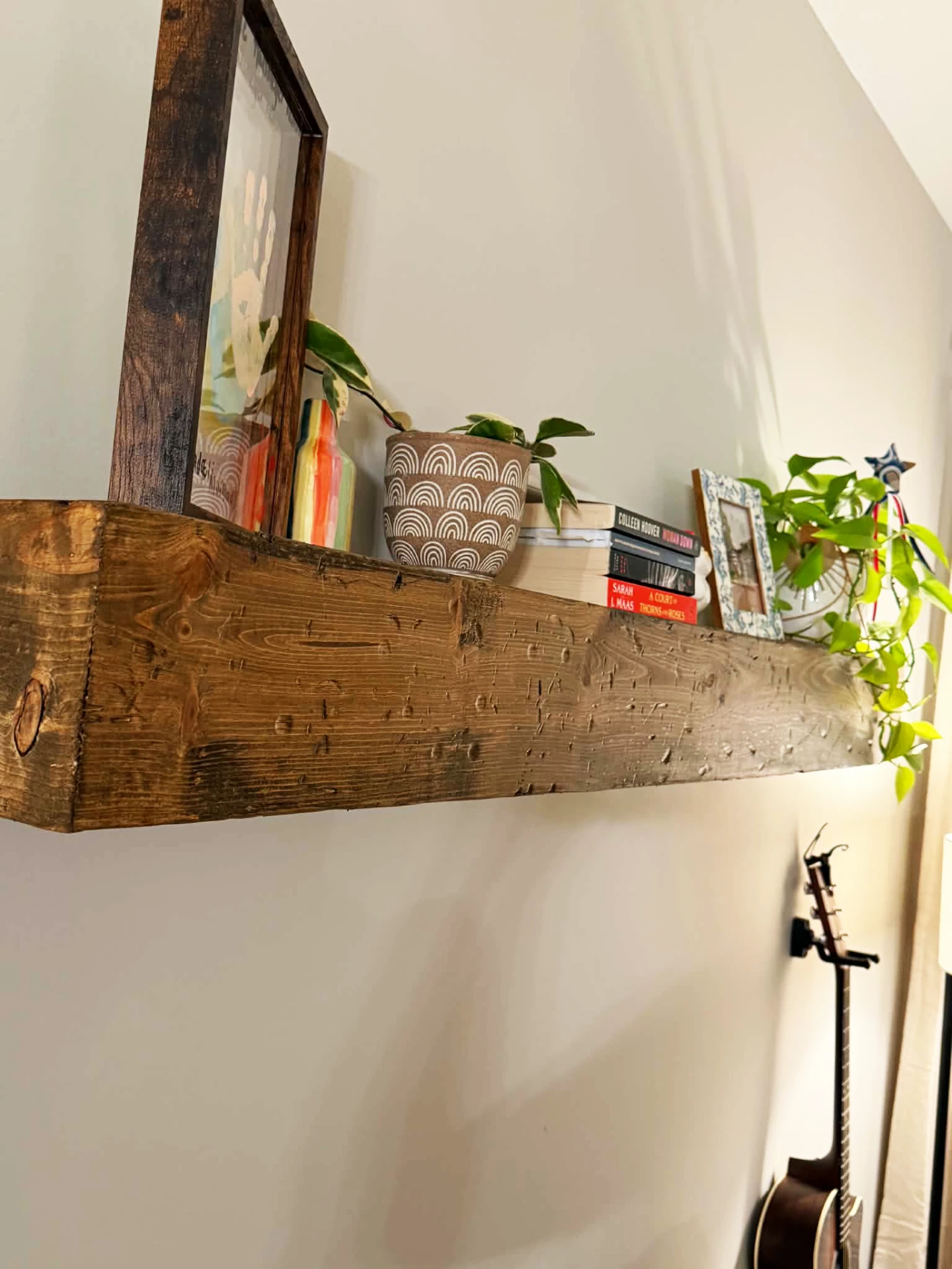 Thick rustic floating shelf displaying plants, books and framed artwork