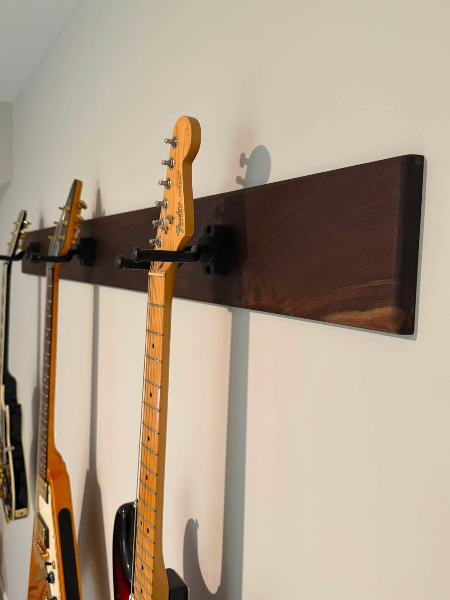 Wall-mounted dark wood guitar rack holding several guitars