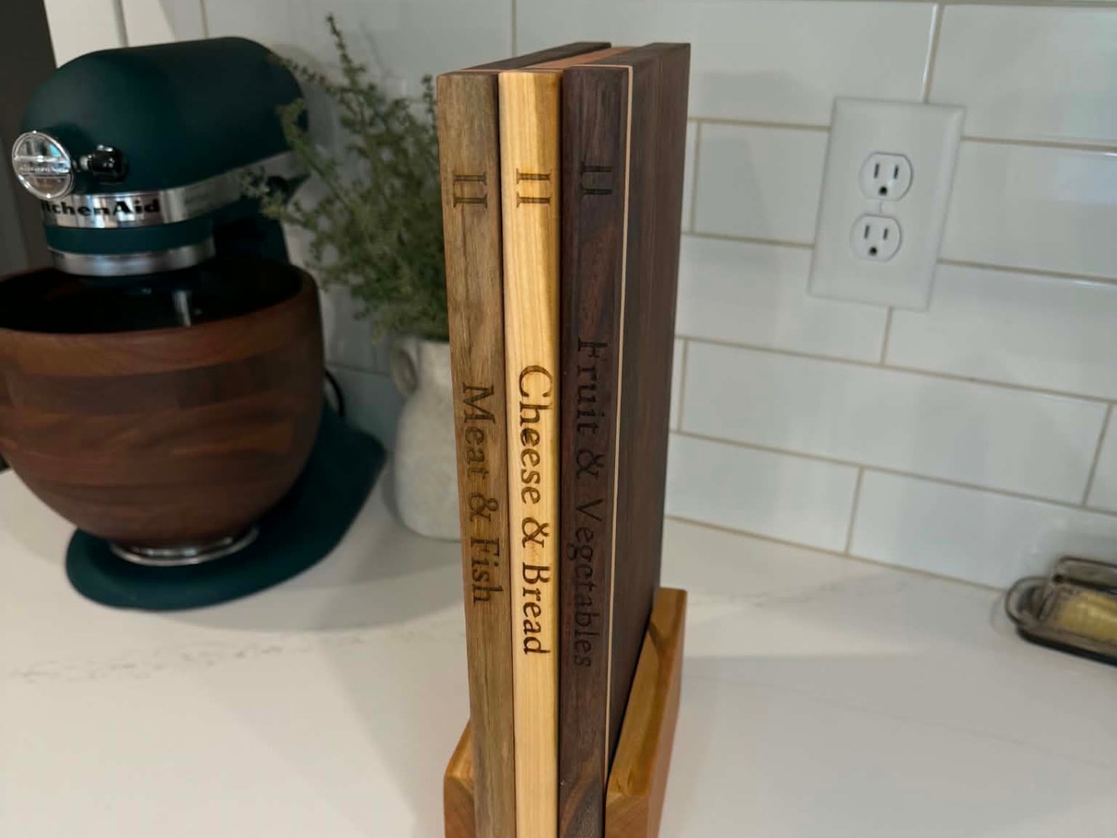 Three engraved hardwood cutting boards standing upright in a cherry stand on a kitchen counter